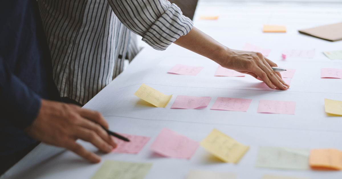 Mani che organizzano post-it su un tavolo durante una sessione di progettazione didattica