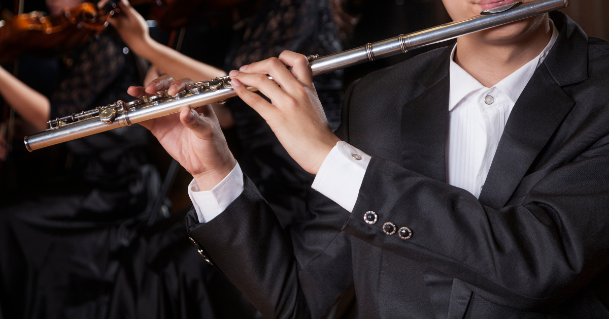 Musicista che suona il flauto traverso in concerto con orchestra sullo sfondo