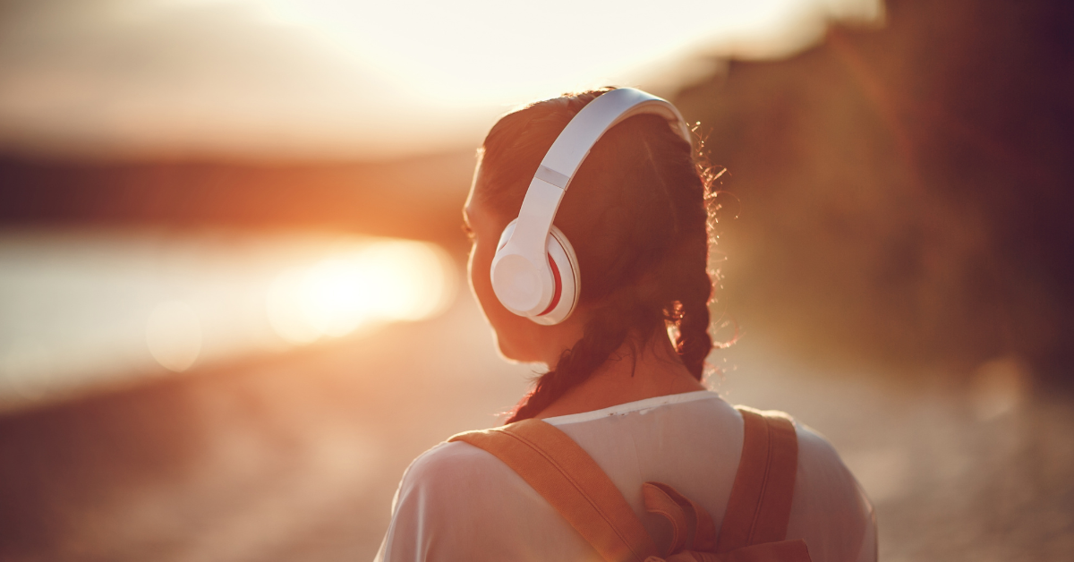 Ragazza che ascolta musica con cuffie al tramonto vicino al mare
