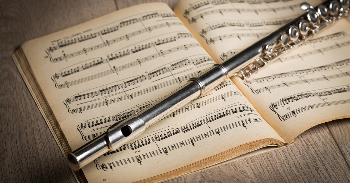 Flauto traverso in metallo appoggiato su uno spartito aperto, simbolo di studio e formazione musicale.
