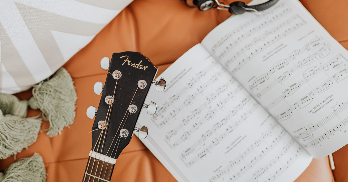 Chitarra acustica accanto a uno spartito aperto, simbolo di studio e apprendimento musicale.